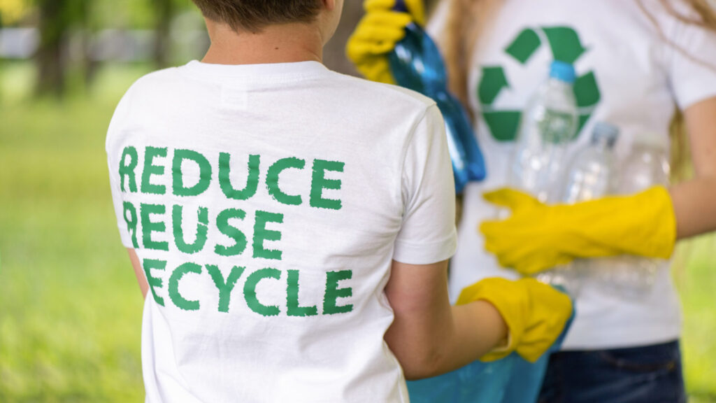two people collecting plastic in a bag in a polluted park. Close view of recycling signs on T-shirts